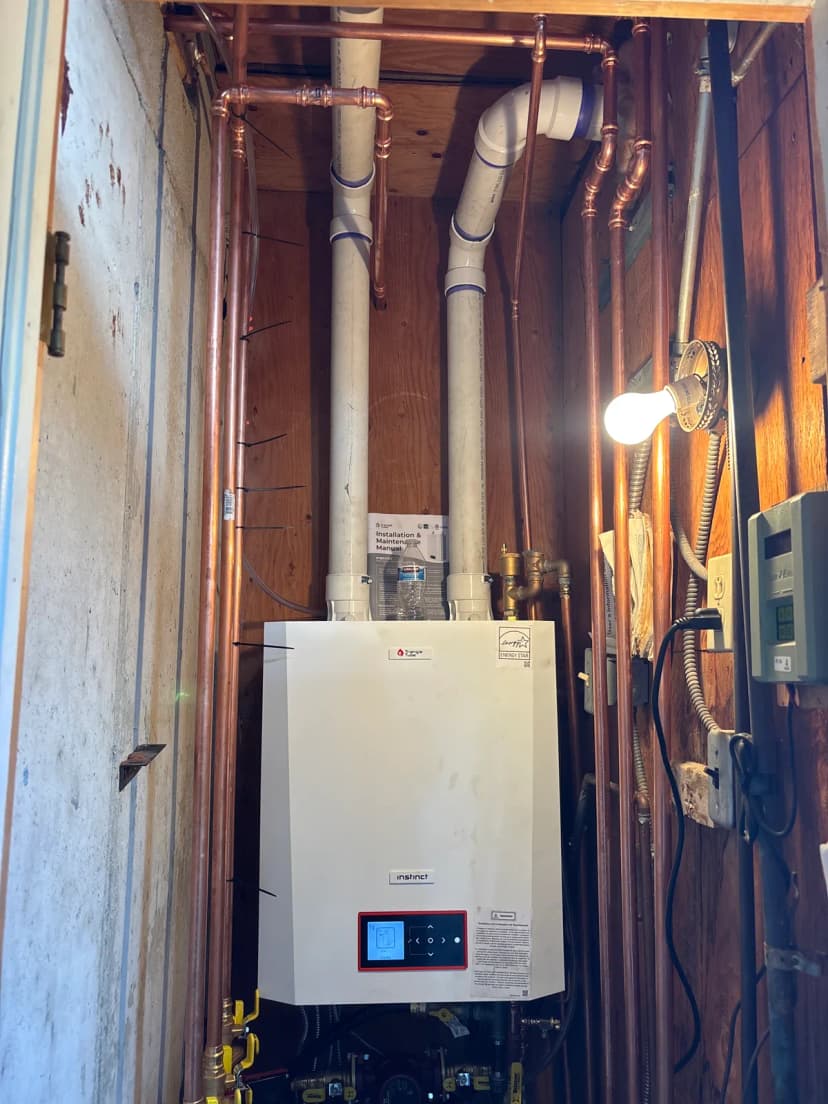 A white wall-hung boiler in a closet with two white PVC vent pipes above it and new copper piping on both sides.