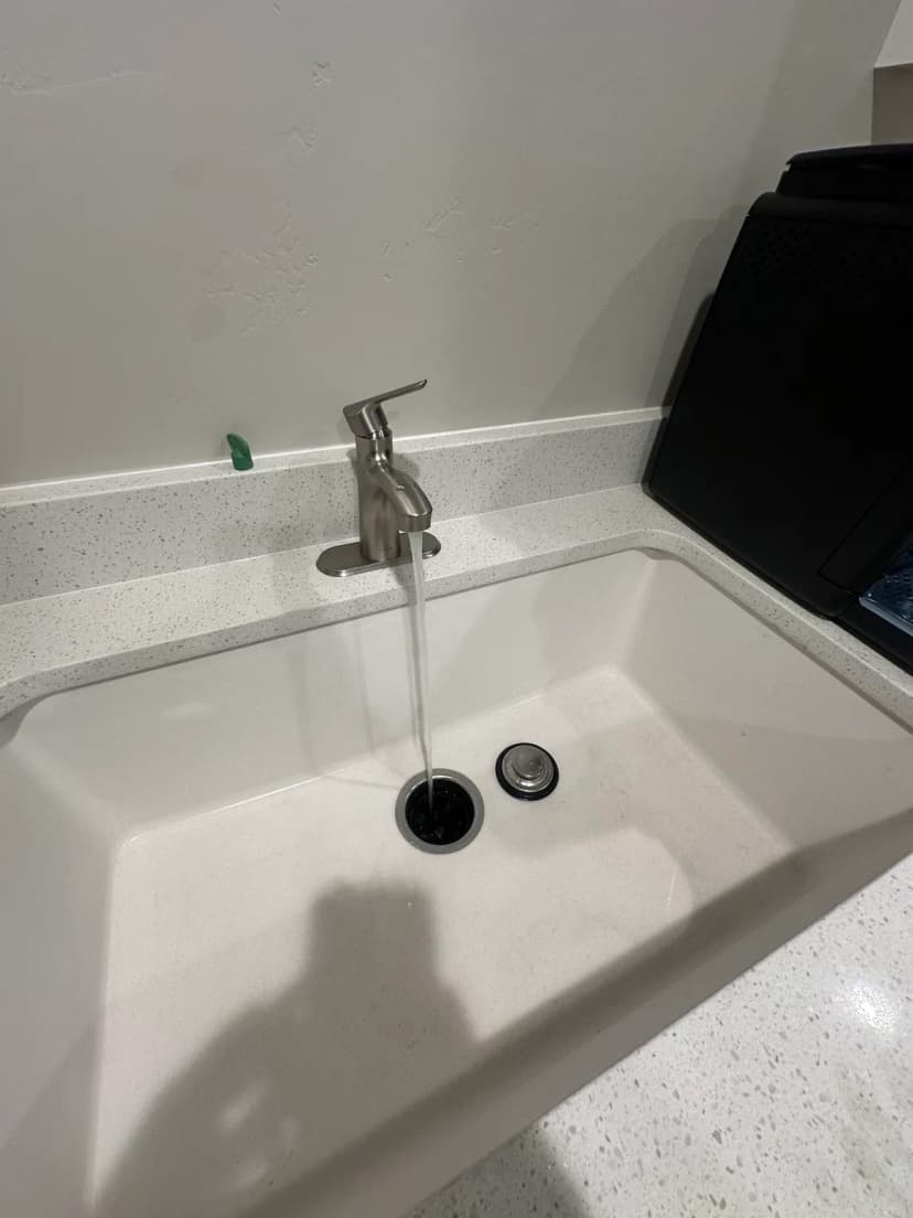 Water running from a brushed single-handle faucet into a white sink set in a speckled countertop.
