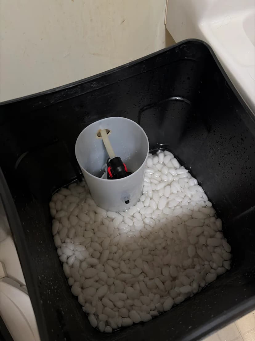 Looking down into a black brine tank with white salt pellets around a gray tube that holds the float.