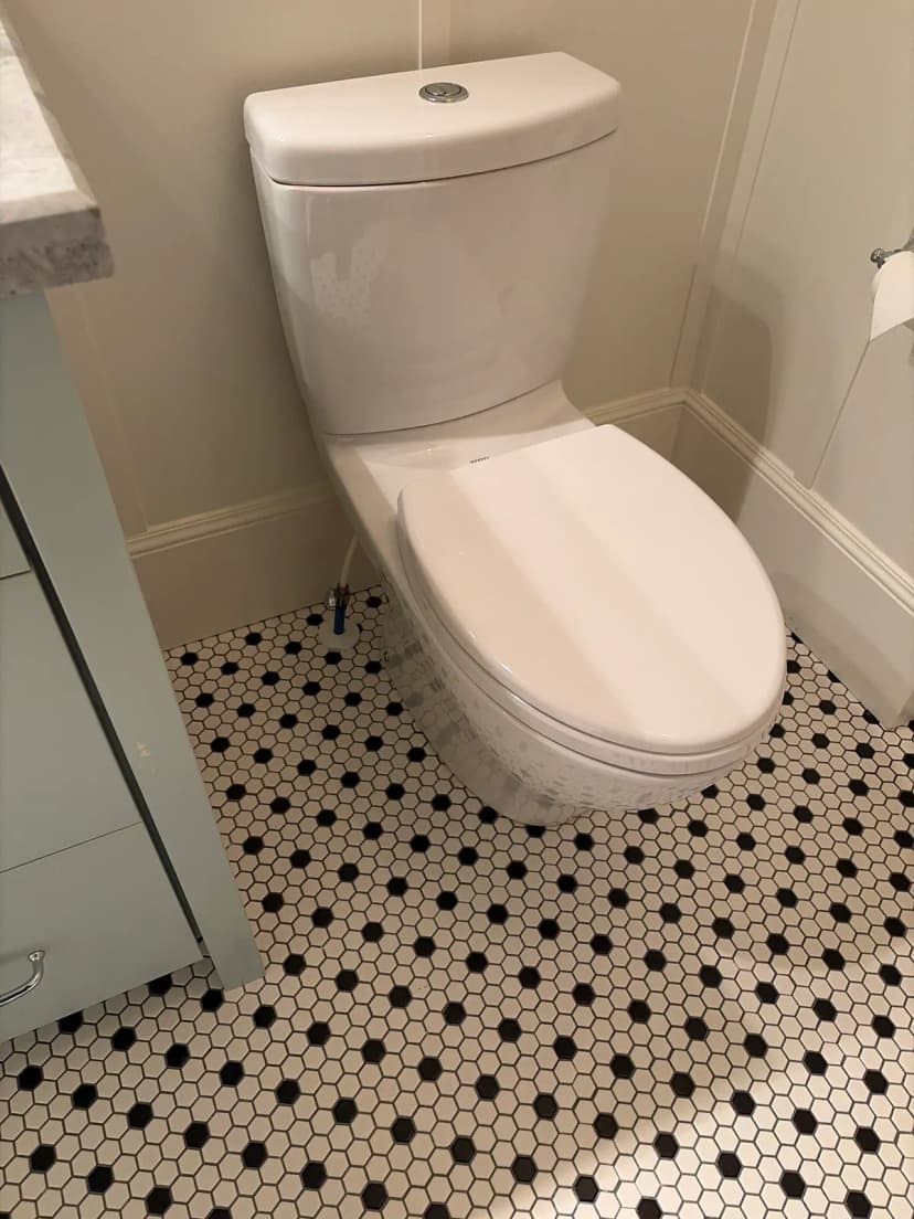 A white toilet on a black-and-white hexagon tile floor.