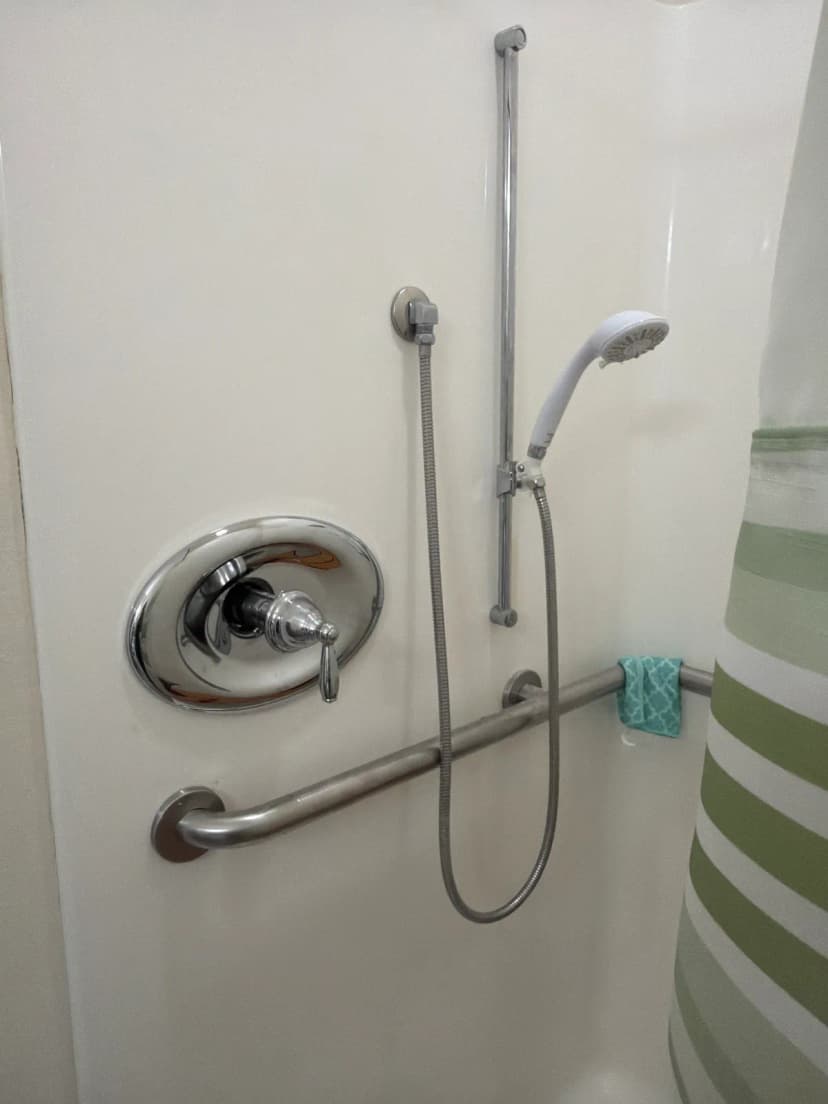 A chrome shower valve handle with a handheld shower on a slide bar and a grab bar.