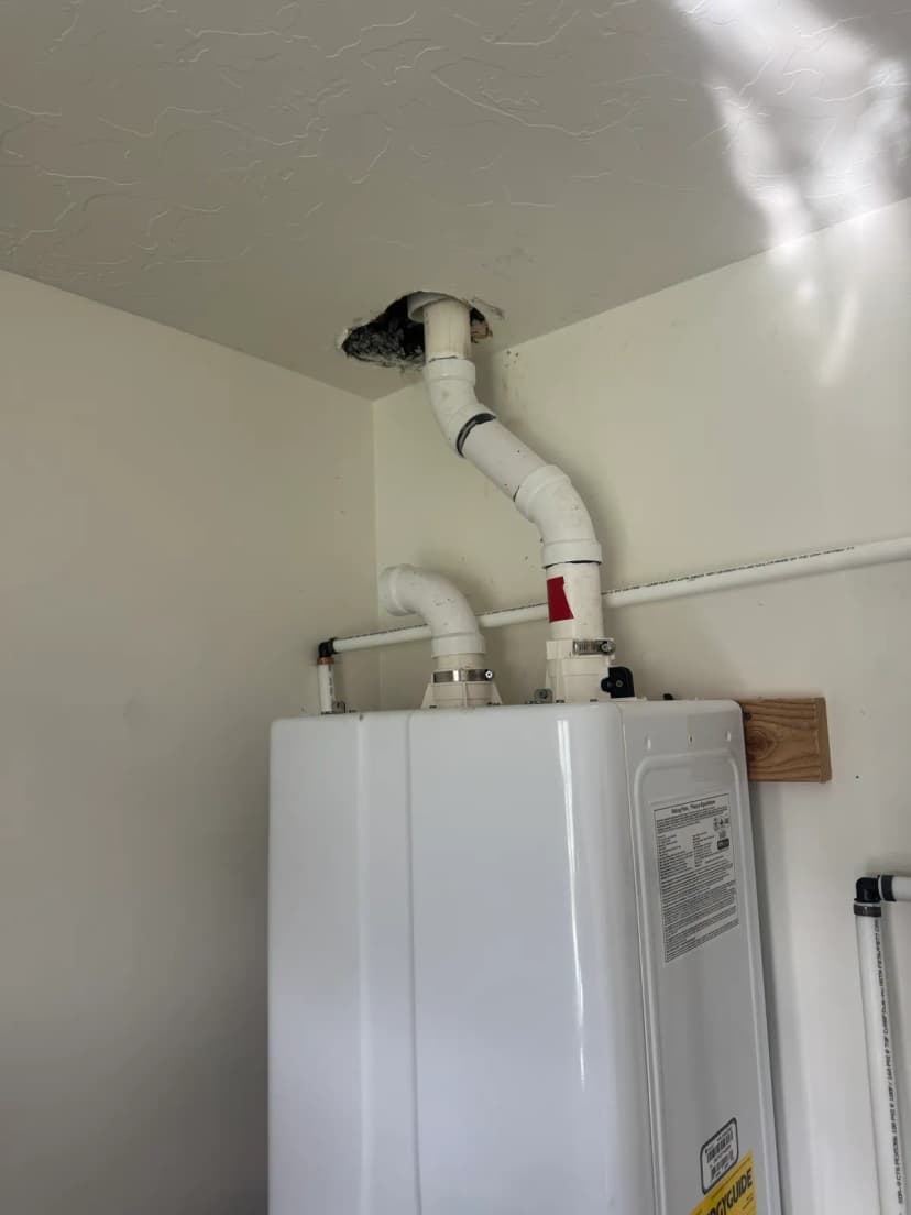 A white tankless water heater on a wall, with white vent pipes rising to the ceiling.