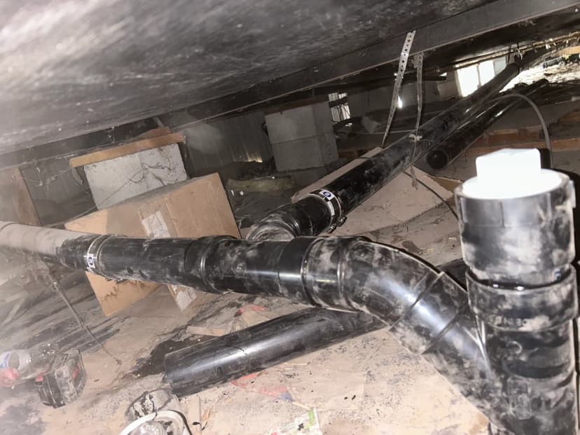 Black ABS drain pipes and fittings in a crawl space under a home.