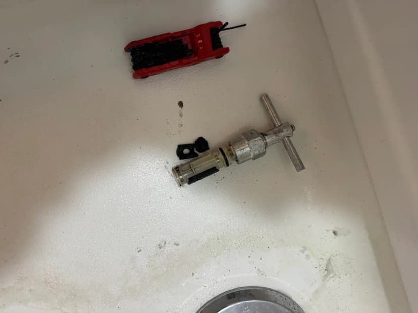 A shower valve cartridge and a puller tool lying in a white bathtub.