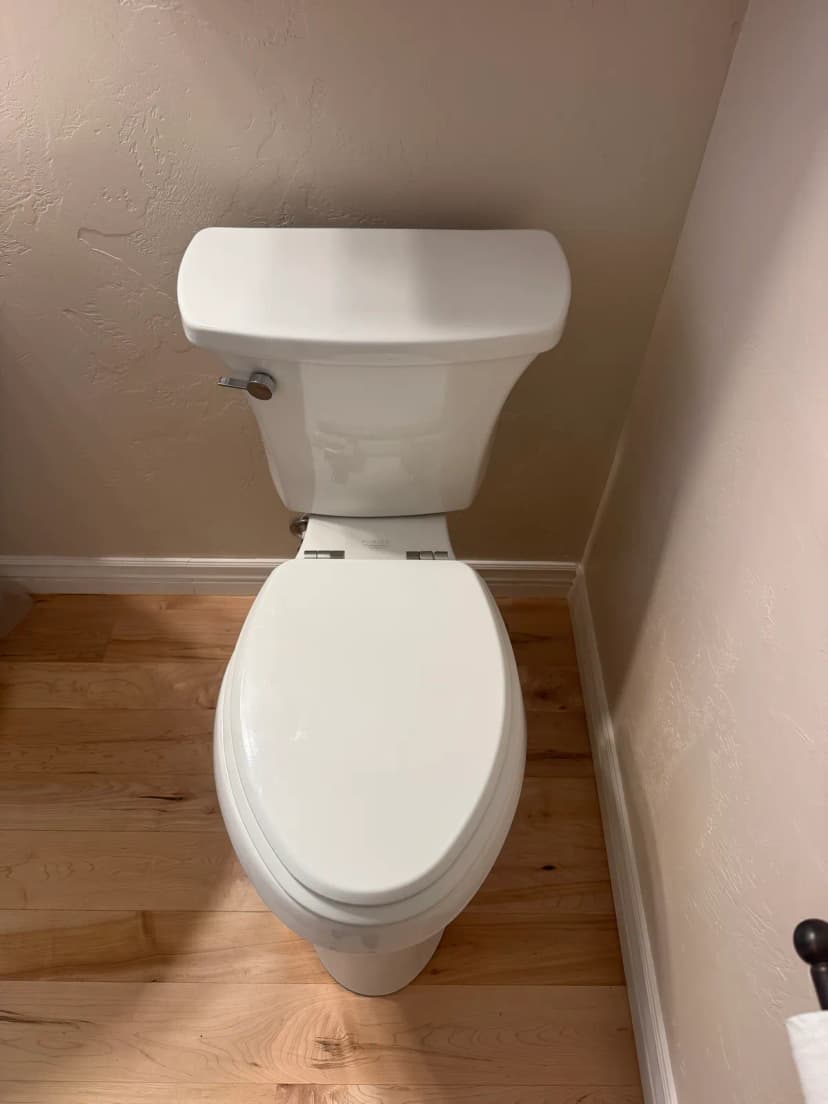 A white toilet against a wall on a wood floor.