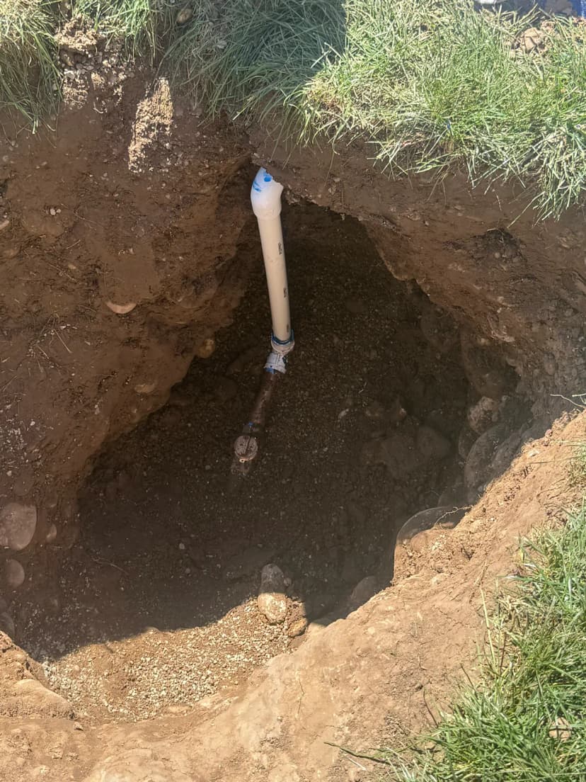 A hole dug in a lawn with a white pipe rising from a valve at the bottom.