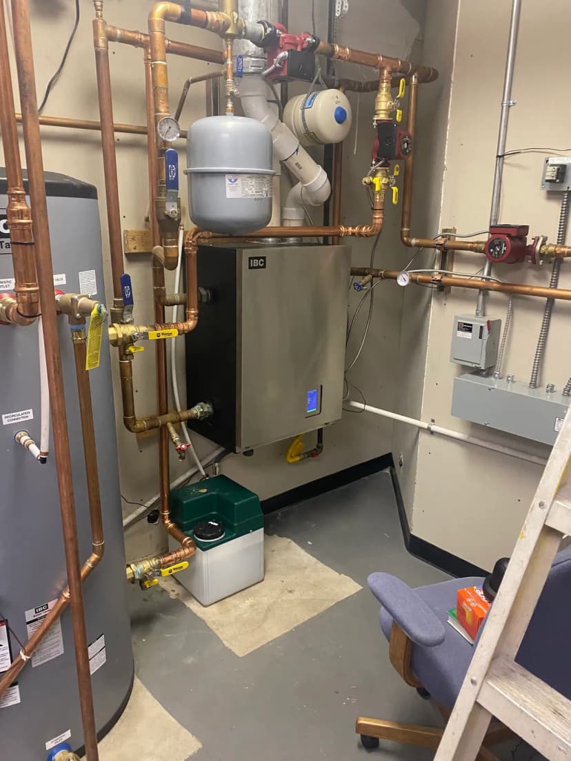 A wall-hung boiler with copper piping, an expansion tank, and a circulator pump in a mechanical room.