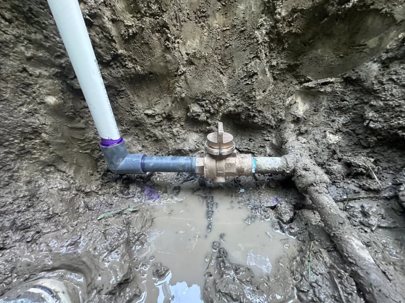 A brass valve joined to plastic pipe at the bottom of a muddy hole.