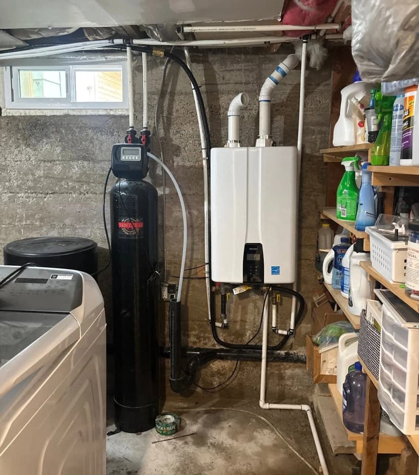 A wall-mounted tankless water heater beside a water softener tank on a concrete basement wall.