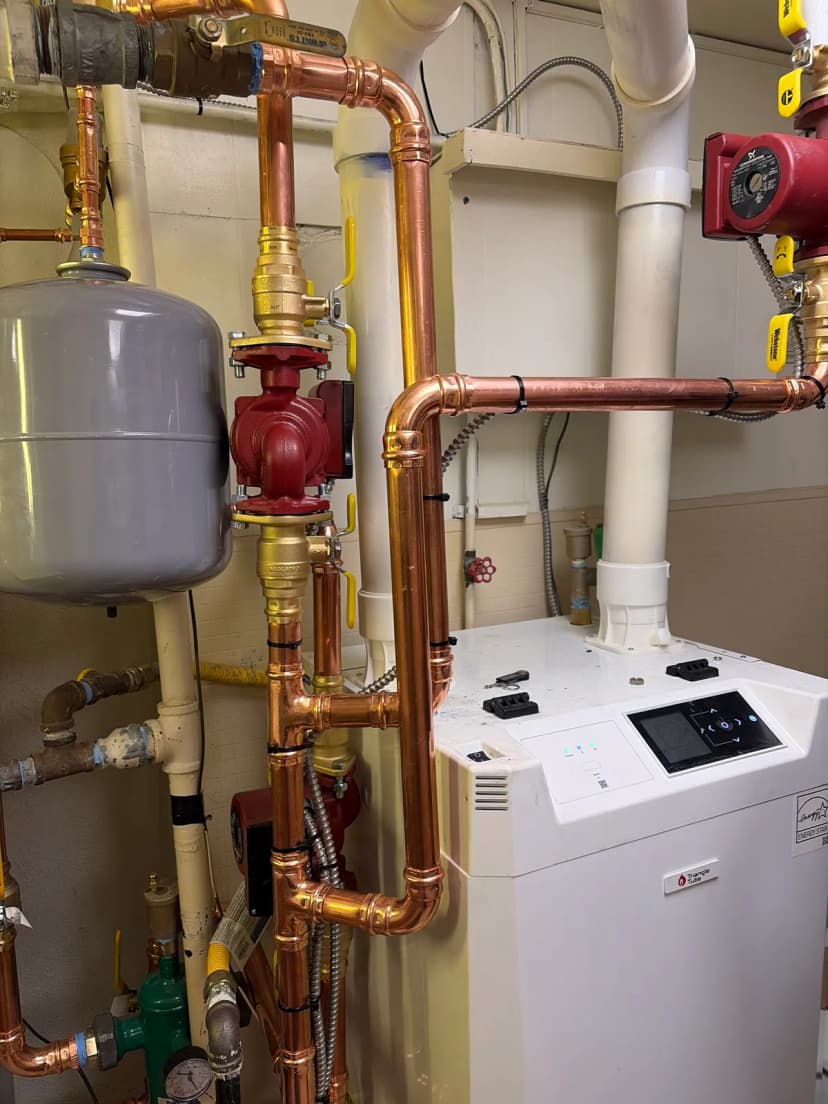 Copper pipes, a red pump with yellow-handled valves, and a gray expansion tank beside a white boiler.