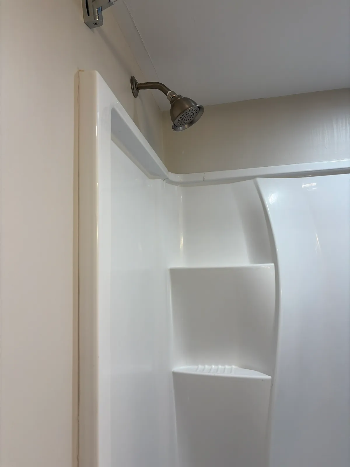 A brushed nickel shower arm and shower head above a white shower surround.