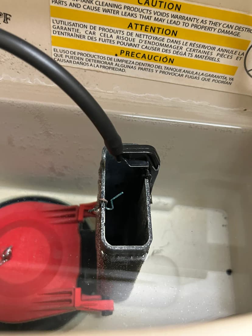The inside of a toilet tank with a red flapper and a black fill valve.