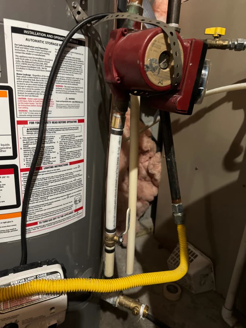 A red recirculation pump beside a gas water heater, with white PEX pipe and a shut-off valve below it.